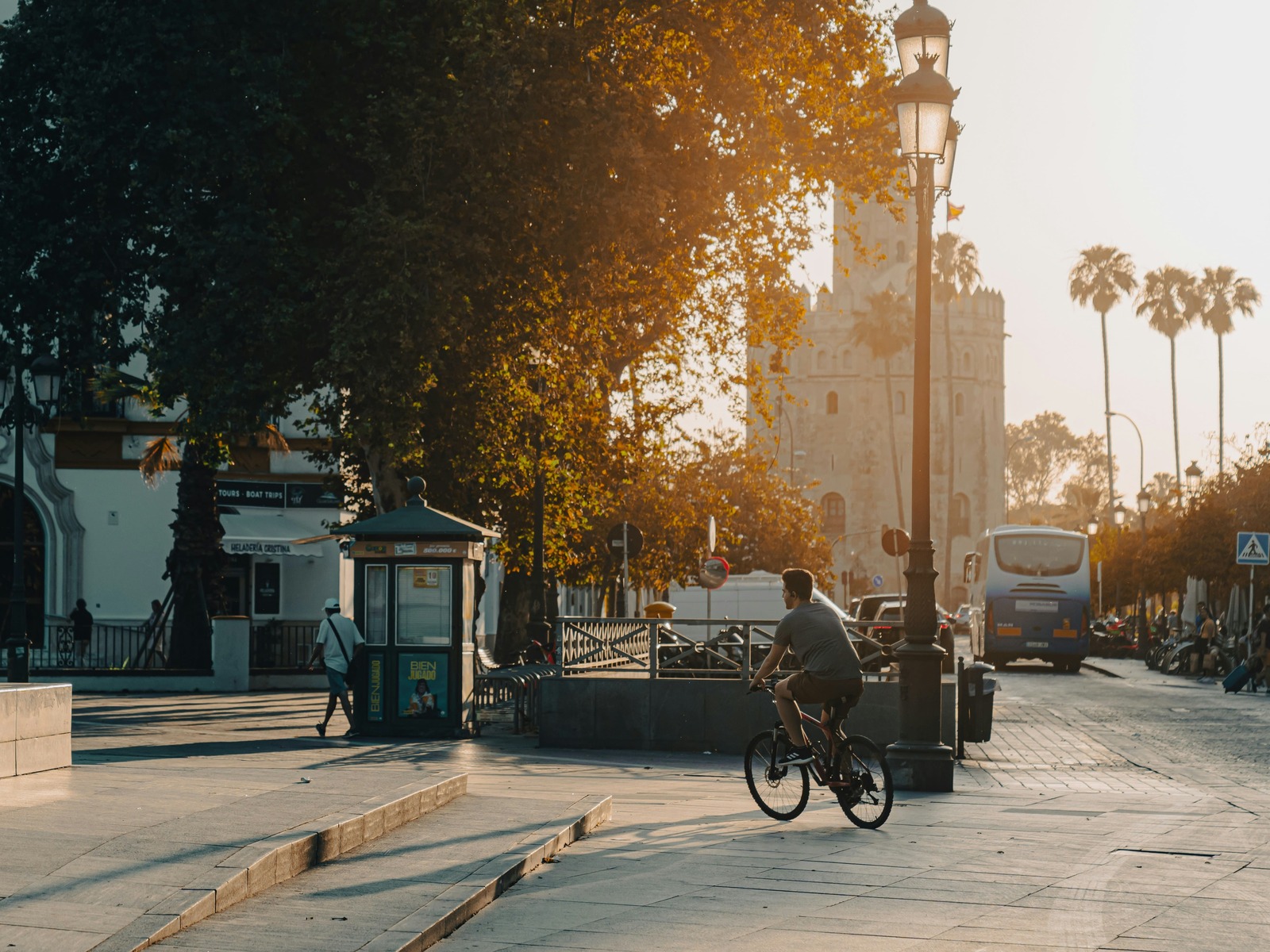 Un ciclista recorre el paseo peatonal junto a la Torre del Oro de Sevilla bajo la luz dorada del atardecer