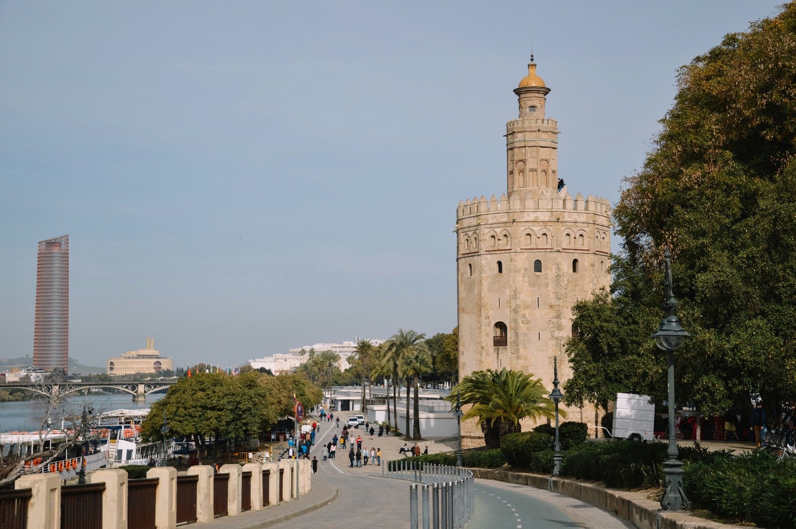Paseo junto al muelle con peatones, el Puente de Triana y la Torre Sevilla en el horizonte
