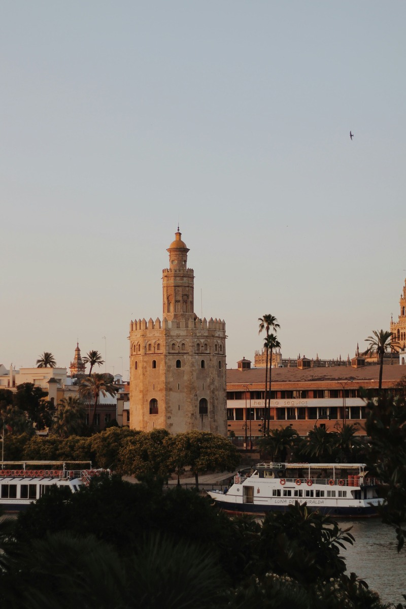 Silueta de la Torre del Oro y la ciudad al anochecer con barcos navegando por el río