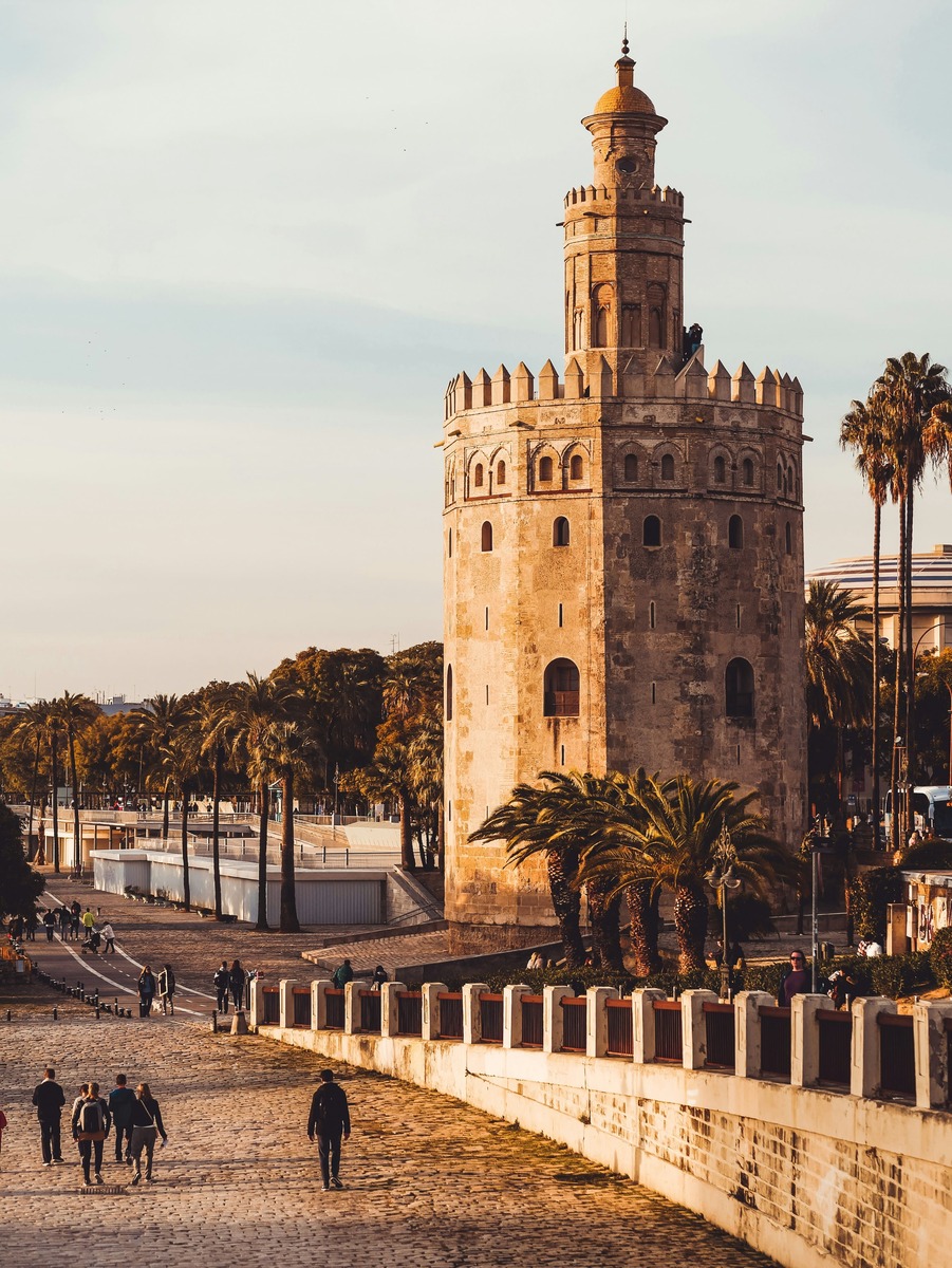 Perspectiva elevada de la rampa de acceso al muelle de la Torre del Oro con visitantes al atardecer